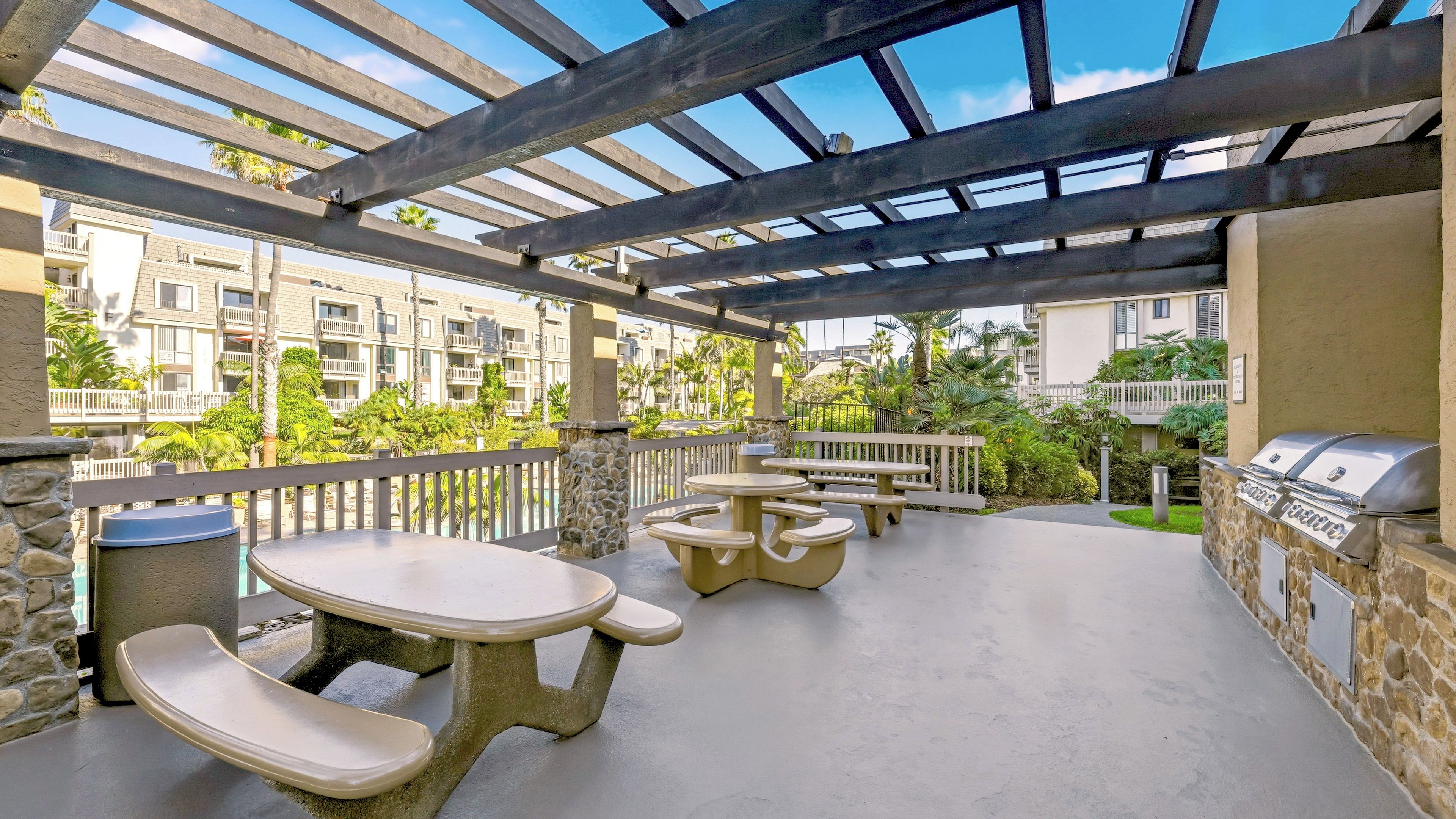 An outdoor patio with stone tables and benches, a grill, and a view of residential buildings.