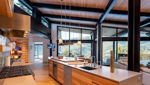 A modern kitchen with a large island, wooden cabinetry, and a view of the outdoors. - Chalet La Forja - Ski in Ski out Kadenwood Estate (Whistler)