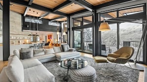 A modern living room with a sectional sofa, a round coffee table, and a view of a snowy landscape through large windows. - Chalet La Forja - Ski in Ski out Kadenwood Estate (Whistler)