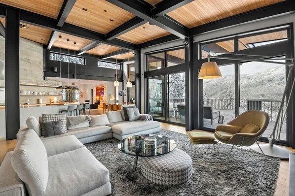 Ein modernes Wohnzimmer mit einem Ecksofa, einem runden Couchtisch und Blick auf eine verschneite Landschaft durch große Fenster.