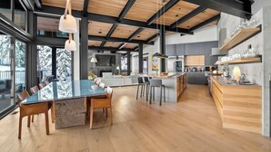 A spacious modern kitchen with a large island, wooden beams, and a view of snow-covered trees. - Chalet La Forja - Ski in Ski out Kadenwood Estate (Whistler)