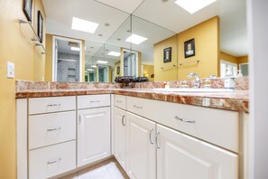 A bathroom with a marble countertop, white cabinets, a large mirror, and a yellow accent wall.