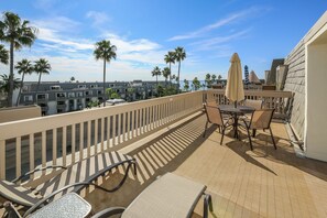 A balcony with outdoor furniture, a view of palm trees, and a building in the background.