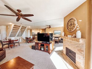 A spacious living room with a fireplace, a large flat-screen TV, and a dining area with wooden furniture. - Upscale 2 Story Penthouse- Beautiful Tropical garden and ocean views  - G322 North Coast Village (Oceanside)