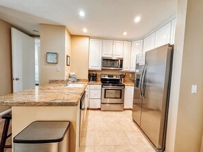 A kitchen with white cabinets, stainless steel appliances, a granite countertop, and a small bar stool. - Upscale 2 Story Penthouse- Beautiful Tropical garden and ocean views  - G322 North Coast Village (Oceanside)