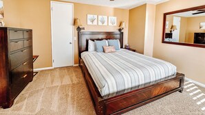 Une chambre à coucher avec un lit, une commode, un ventilateur de plafond et un miroir au mur.
