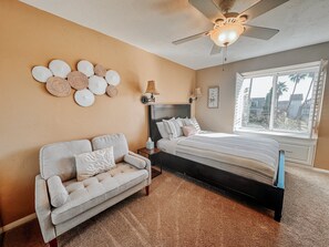 A bedroom with a bed, a sofa, a ceiling fan, a window with blinds, and wall decor. - Upscale 2 Story Penthouse- Beautiful Tropical garden and ocean views  - G322 North Coast Village (Oceanside)