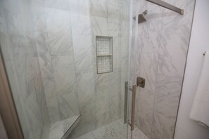 A glass-enclosed shower with a white marble wall, a small window, and a towel rack.