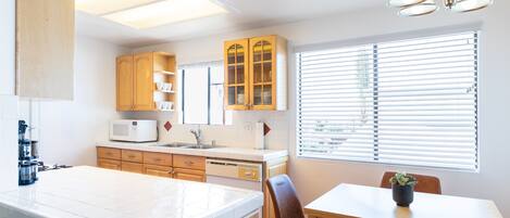 A kitchen with a central island, wooden cabinets, a microwave, and a dining area with chairs and a table.