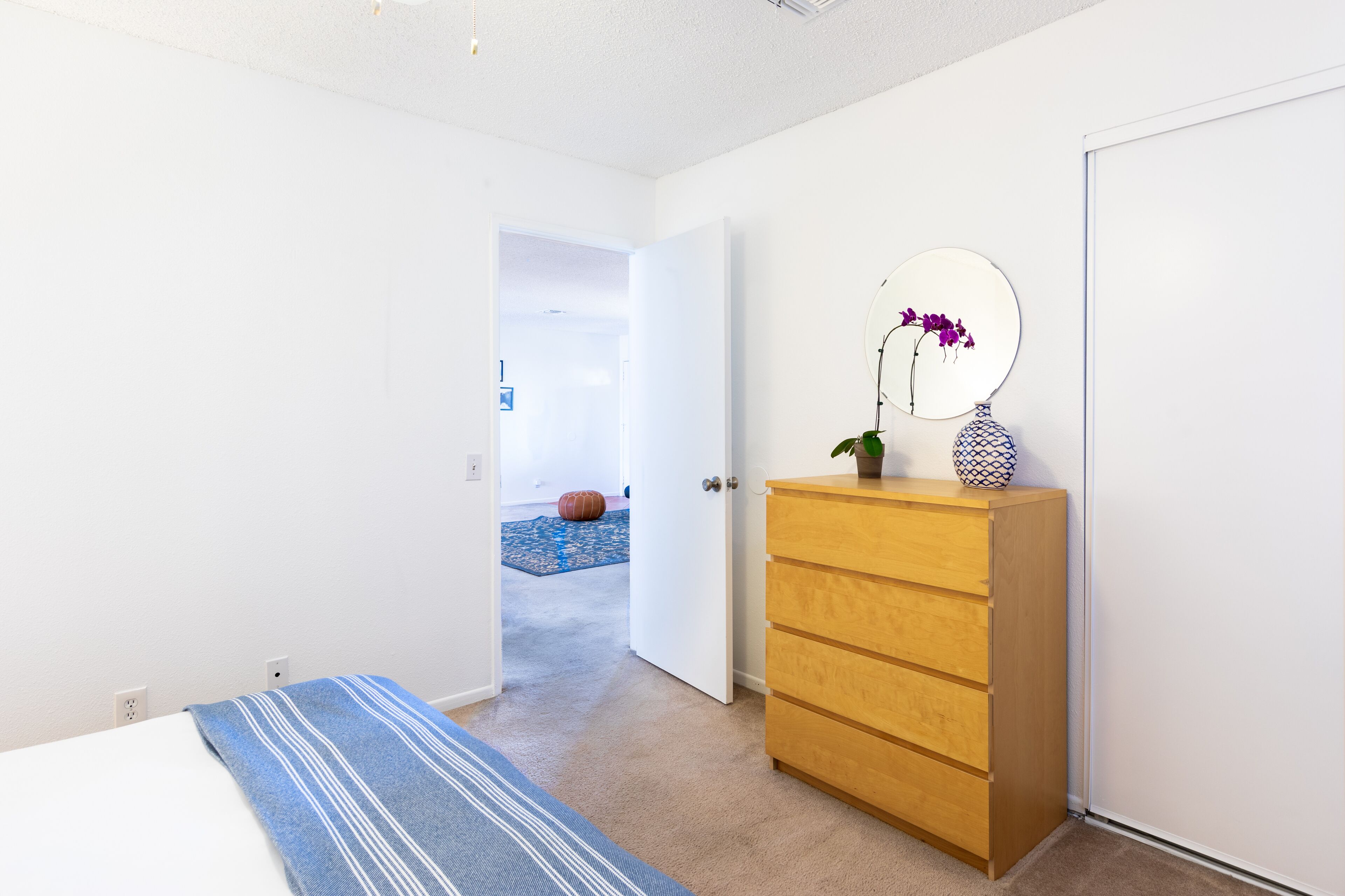 Une chambre à coucher comprenant un lit, une commode en bois, un miroir et une porte donnant sur une autre pièce.