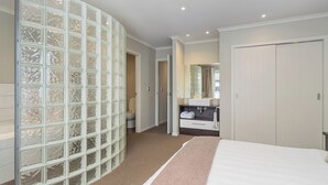 Une chambre d’hôtel avec un grand lit, une salle de bain avec un lavabo et un miroir, et une porte-fenêtre coulissante donnant sur une autre pièce.