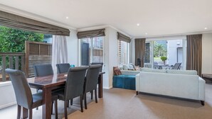Un salon moderne avec un coin repas, de grandes fenêtres et une vue sur l’extérieur.