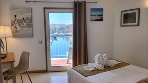 Une chambre d’hôtel comprenant un lit, un bureau, une chaise, un balcon avec vue sur la ville et des œuvres d’art accrochées aux murs.