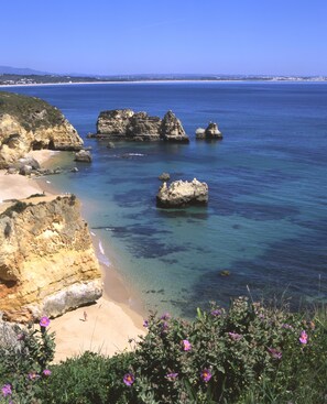 Un paysage côtier caractérisé par une eau d’un bleu limpide, des falaises rocheuses et une plage de sable.