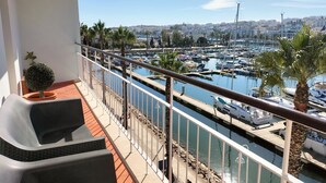 Un balcon offrant une vue sur une marina, avec des bateaux et un paysage urbain lointain.