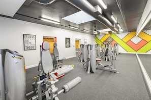 Een sportschool met diverse fitnessapparaten, motiverende posters en een kleurrijk wandontwerp.