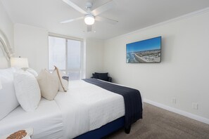 A bedroom with a bed, a ceiling fan, a window, a wall-mounted TV, and a beach view painting. - Upper Beachfront-Steps From Water's Edge-D28 North Coast Village (Oceanside)