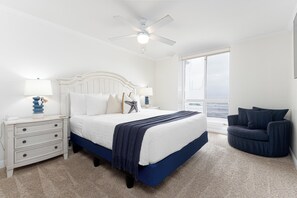 A bedroom with a bed, nightstands, a chair, a ceiling fan, and a large window.