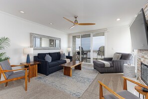A spacious living room with a ceiling fan, a fireplace, and a view of the ocean through large sliding glass doors.