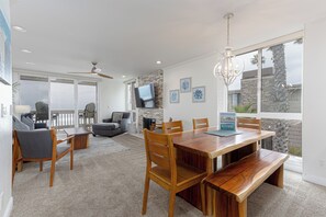 Een ruime eethoek met een houten tafel en stoelen, een aan de muur bevestigde televisie en een uitzicht op de omgeving door grote ramen.