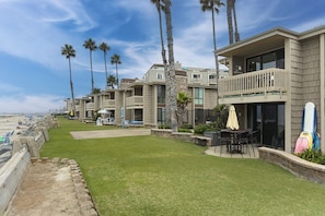 A beachfront property with multiple-story buildings, outdoor seating areas, and a view of the ocean.