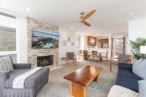 A spacious living room with a stone fireplace, a ceiling fan, and a large TV mounted on the wall.