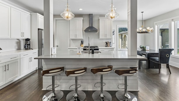 A modern kitchen with white cabinetry, a central island with bar stools, pendant lighting, and a view to the dining area. - Rooftop Style · Fire Pit · Wet Bar · Skyline Views (Nashville)