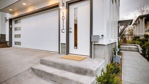A modern residential building with a garage, a front door labeled "101C", and a concrete driveway leading to a set of steps. - Rooftop Style · Fire Pit · Wet Bar · Skyline Views (Nashville)