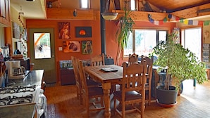 A wooden dining table with chairs, a potted plant, and a stove in a cozy kitchen area. - Pool;wilderness; view of mountains, lake, river;hot tub, sauna;privacy;hiking! (Argenta)
