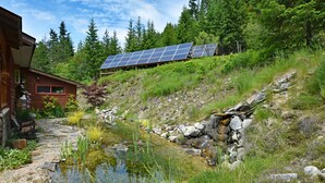 A rustic cabin with solar panels, a pond, and a forested hillside. - Pool;wilderness; view of mountains, lake, river;hot tub, sauna;privacy;hiking! (Argenta)
