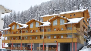 Un immeuble en bois à plusieurs étages, doté de balcons, entouré d’arbres couverts de neige.