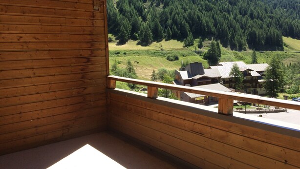 Une cabane en bois dotée d’un balcon donnant sur une vallée boisée et un petit bâtiment.