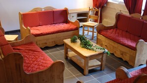 Une pièce chaleureuse, meublée de meubles en bois, notamment un canapé et des fauteuils, ainsi qu’une petite table agrémentée d’une plante.