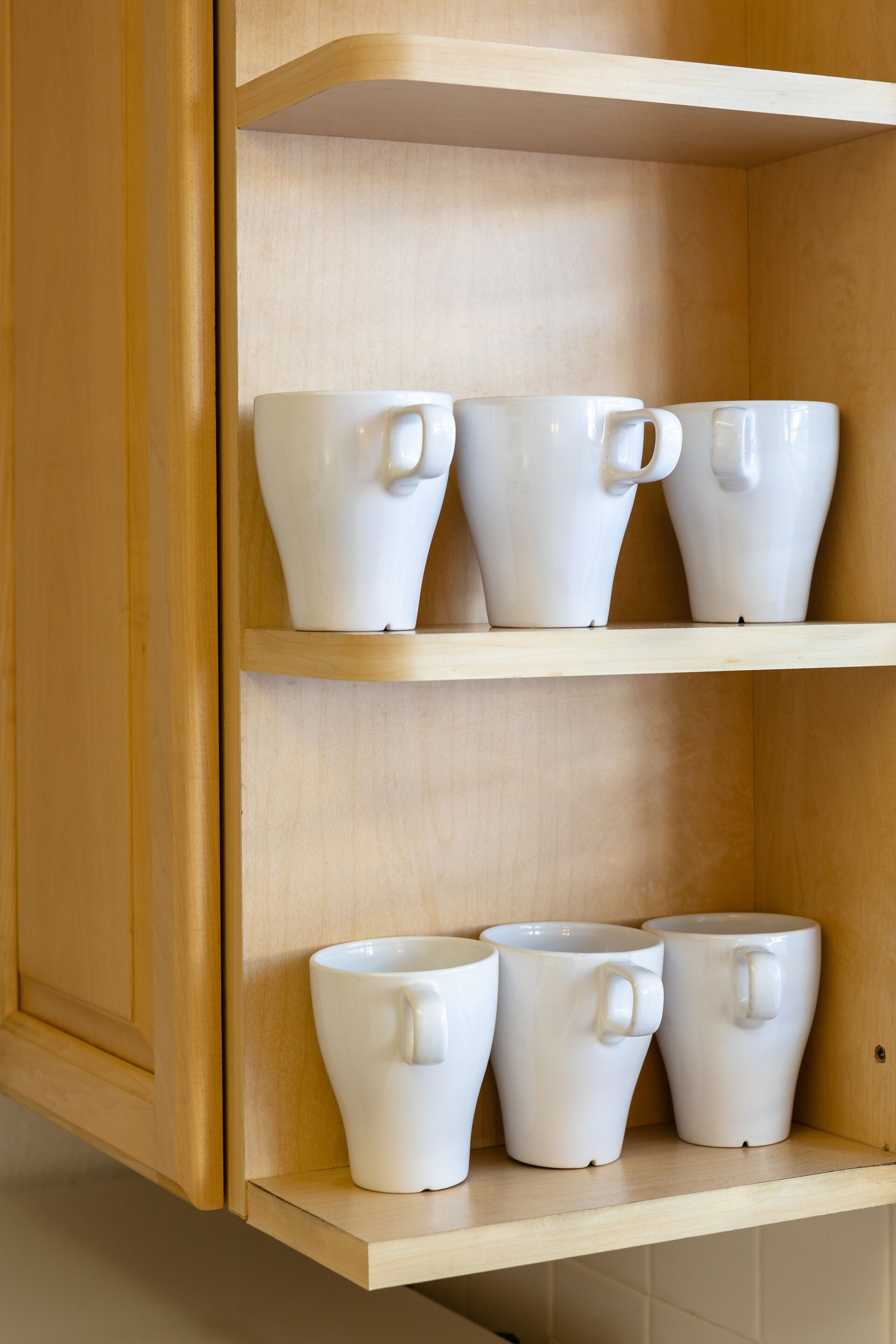 Un mueble de madera con tres estantes, cada uno con tazas de cerámica blanca con asa.