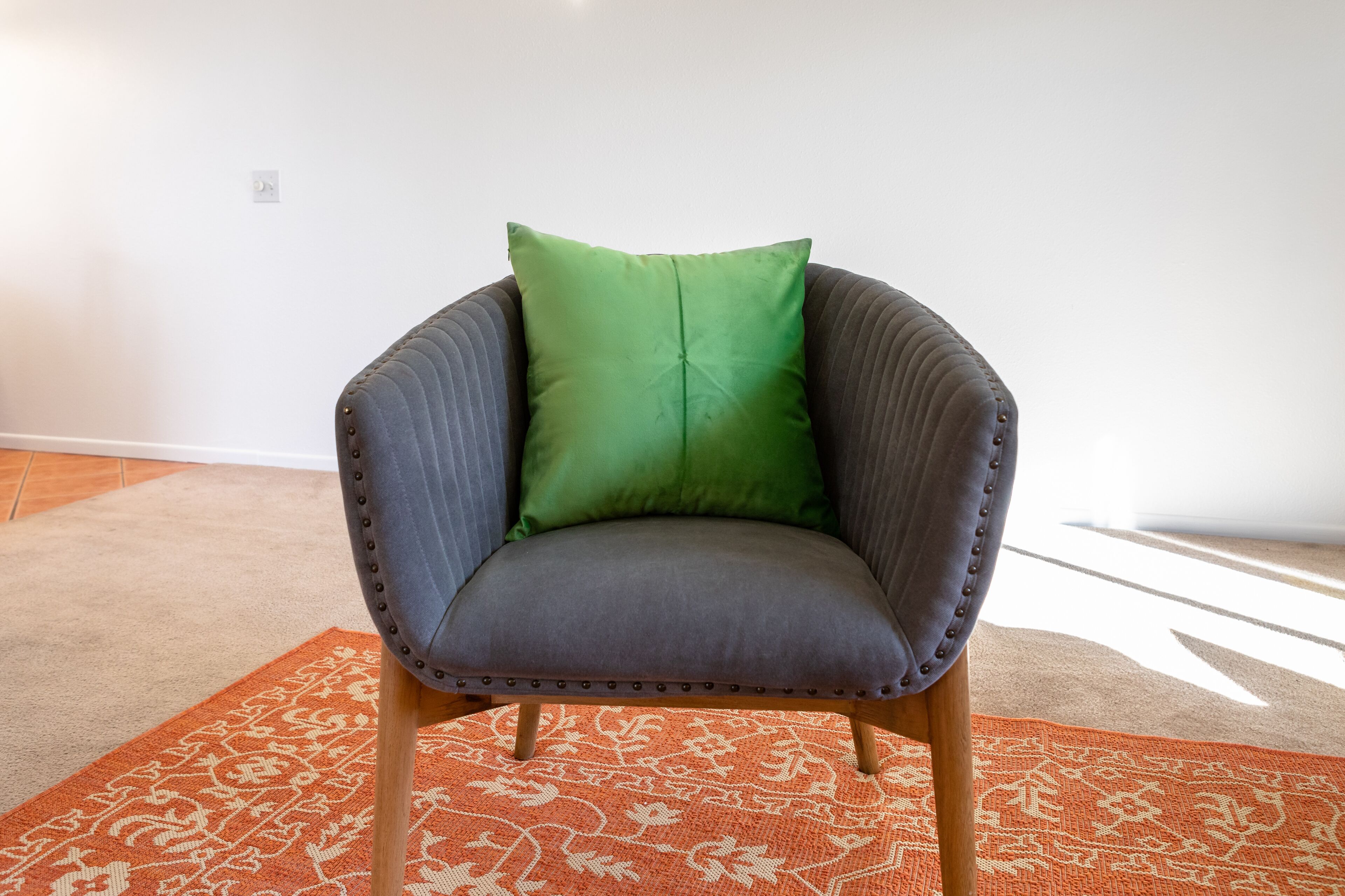 A chair with a green cushion, wooden legs, and a patterned orange rug.