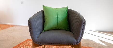 A chair with a green cushion, wooden legs, and a patterned orange rug.