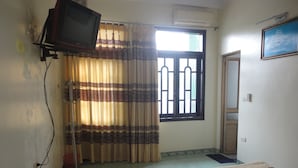A bedroom with a bed, a television mounted on the wall, a window with curtains, and a door. - Thanh Dat Hotel (Ninh Binh)