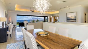 A modern dining area with a wooden table, striped chairs, and a view of the ocean. - Summer Deal Wailea Villa with Ocean Views and Private Lanais (Wailea)