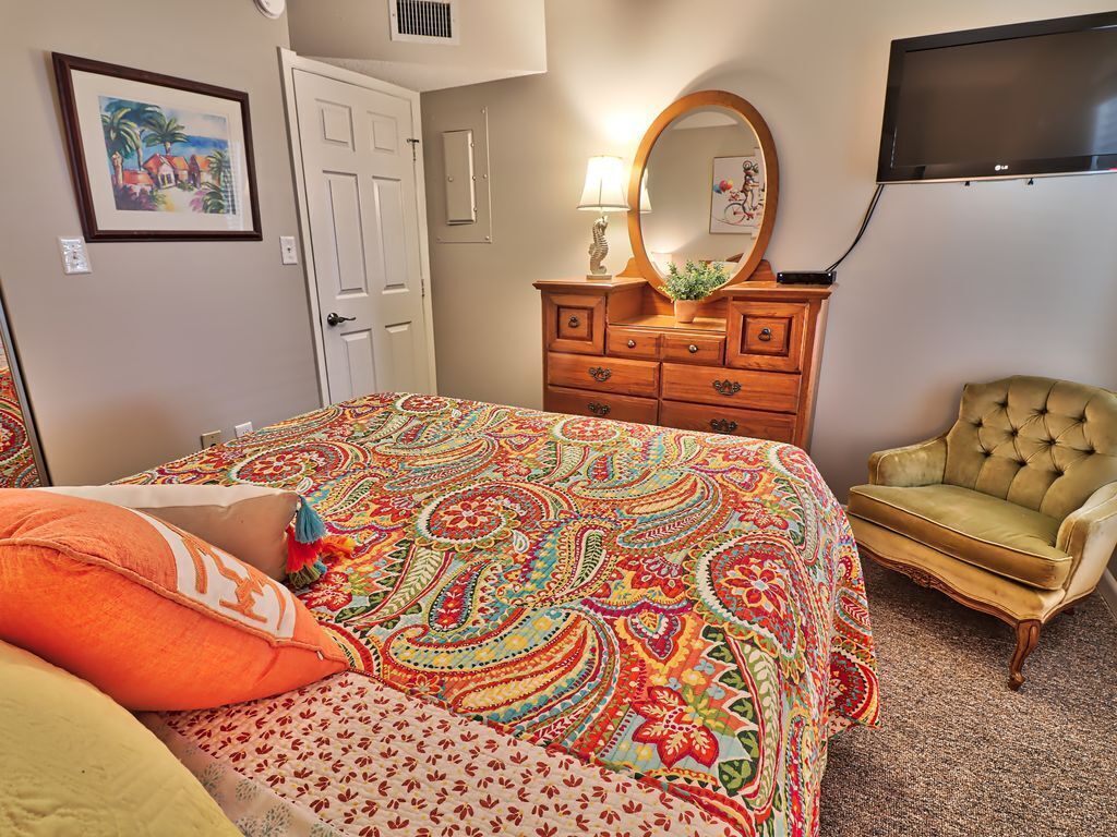 A bedroom with a bed, a dresser, a chair, a TV, and a door.