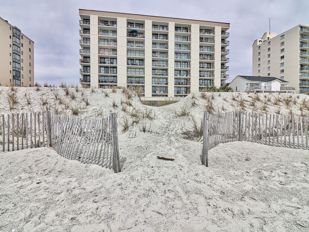 A beachfront hotel with multiple floors, sandy beach in front, and a wooden fence.