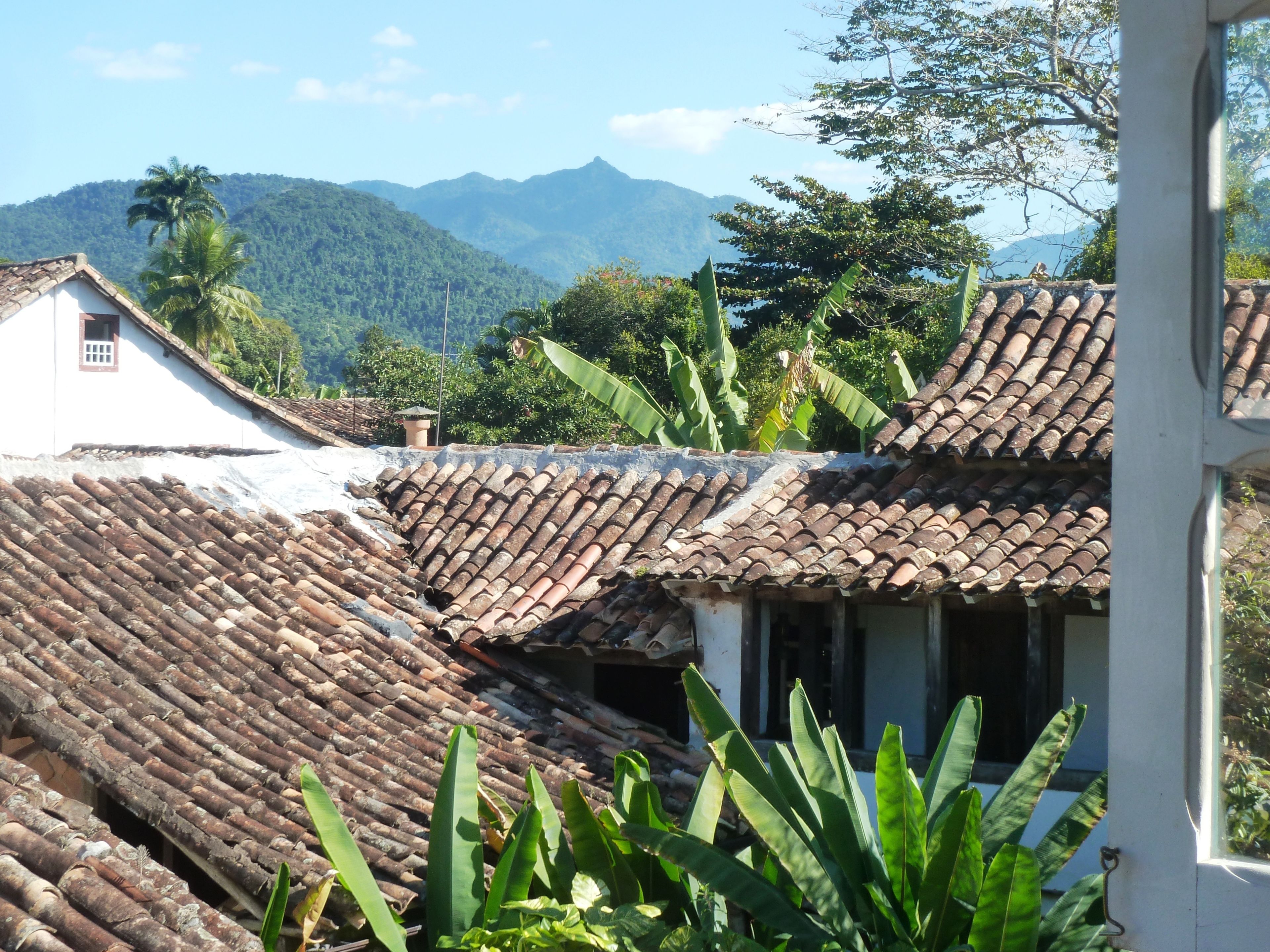 Un bâtiment traditionnel avec un toit en tuiles, entouré d’une végétation luxuriante et avec des montagnes en arrière-plan.