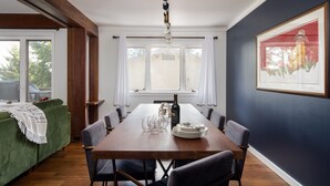 En spiseplads med et træbord dækket til seks personer, omgivet af stole, en grøn sofa og et vindue med gardiner.