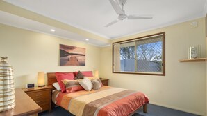 A bedroom with a bed, bedside tables, a lamp, a painting, a window, and a ceiling fan.