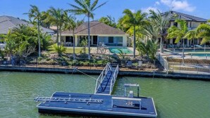 A waterfront property with a dock, palm trees, and houses in the background. - Relaxation & Space in a Canal Home (BANKSIA BEACH)