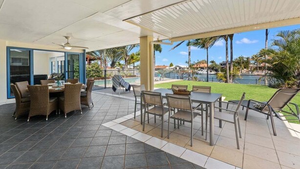 A covered patio area with a dining table and chairs, a pool in the background, and a view of the surrounding landscape. - Relaxation & Space in a Canal Home (BANKSIA BEACH)
