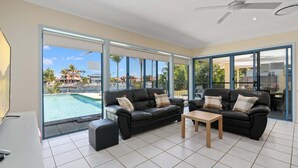 A spacious living room with two black leather sofas, a wooden coffee table, and a large sliding glass door leading to a pool area. - Relaxation & Space in a Canal Home (BANKSIA BEACH)