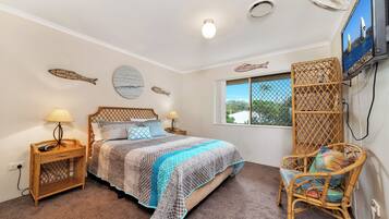 A bedroom with a bed, two bedside tables, a TV, a window, and decorative wall art.