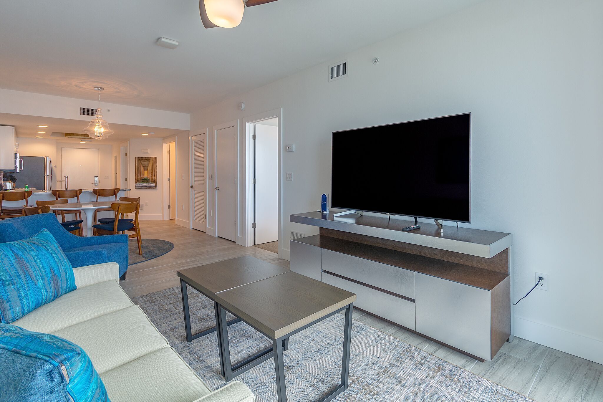 A modern living room with a flat-screen TV, a sofa, a coffee table, and a dining area in the background.