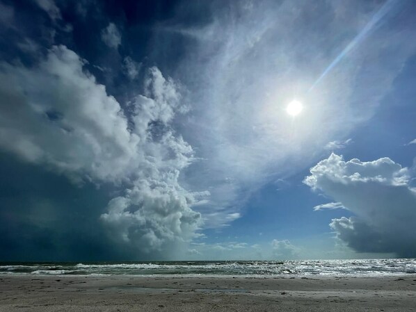 Une plage avec un ciel dégagé et un soleil qui brille à travers les nuages.