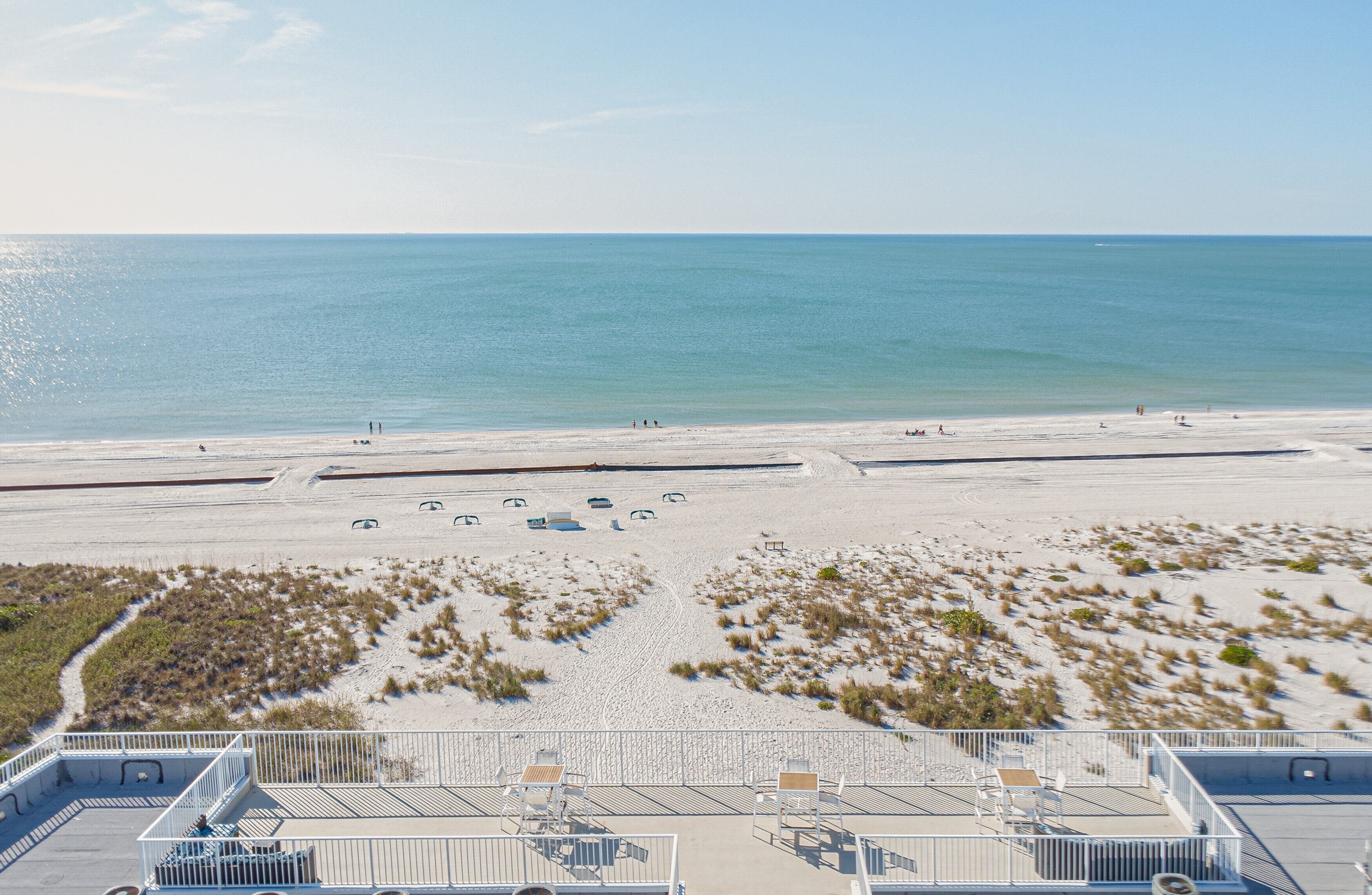 A beach view from a balcony with sun loungers and a railing.